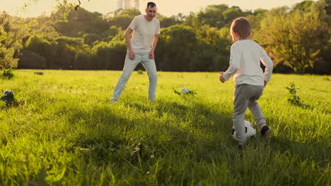 Ein-Junger-Vater-In-Einem-Weißen-T-Shirt-Und-Zwei-Söhne-Spielen-Bei-Sonnenuntergang-In-Der-Sonne-In-Zeitlupe-Fußball-Auf-Dem-Rasen